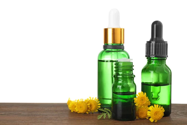 Flessen van kruiden etherische oliën, pipet en bloemen op houten tafel, witte achtergrond — Stockfoto