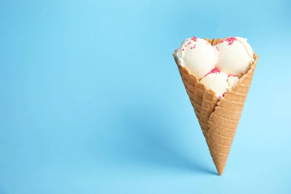 Delicioso helado de vainilla en cono de oblea sobre fondo azul. Espacio para texto — Foto de Stock