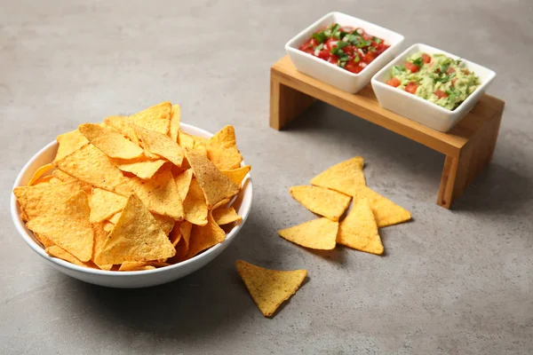 Bowl of delicious mexican nachos chips served with sauces on grey table — Stock Photo, Image