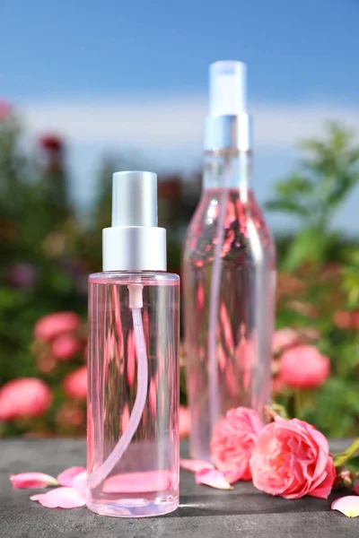 Flaschen Gesichtswasser mit ätherischem Öl und frischen Rosen auf dem Tisch vor verschwommenem Hintergrund — Stockfoto