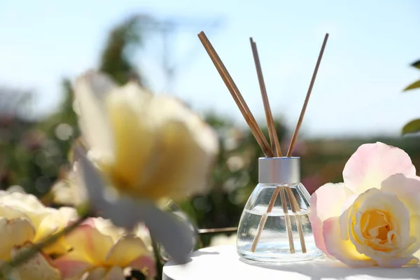 Reed ambientador com óleo e rosa fresca na mesa contra fundo turvo. Espaço para texto — Fotografia de Stock