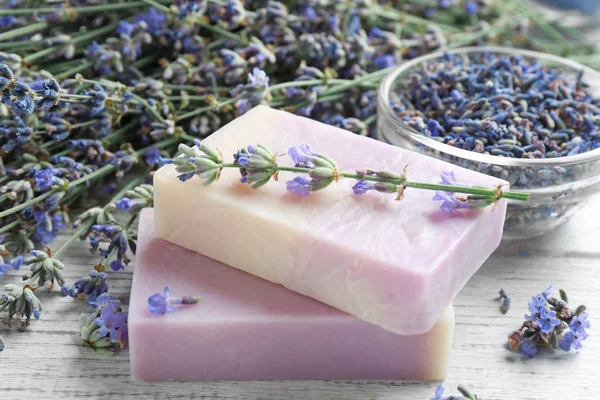 Handmade soap bars with lavender flowers on white wooden table, closeup