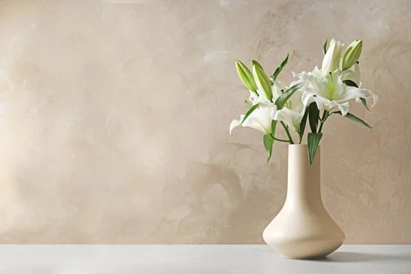 Vaso com lindos lírios na mesa contra fundo marrom claro, espaço para texto — Fotografia de Stock