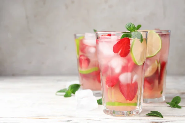 Vasos de bebida refrescante con fresa, lima y menta sobre mesa de madera clara sobre fondo gris, espacio para texto —  Fotos de Stock