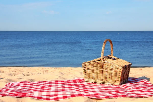 Prosluněná přikrývka s piknikovým košíkem na slunečné pláži. Místo pro text — Stock fotografie