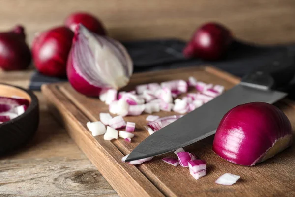 Tabla con cebolla roja cortada y cuchillo en mesa de madera —  Fotos de Stock