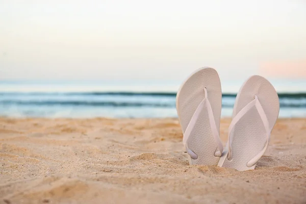 Chanclas blancas sobre arena cerca del mar, espacio para el texto. Accesorios de playa —  Fotos de Stock
