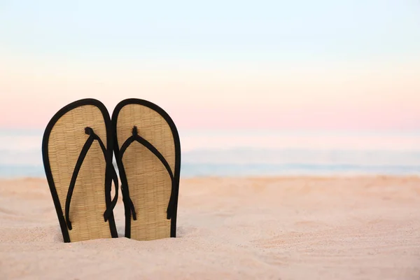 Stijlvolle flip flops op zand in de buurt van zee, ruimte voor tekst. Strand accessoires — Stockfoto