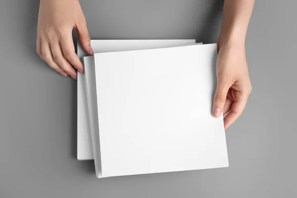 Mujer sosteniendo hojas de papel en blanco para folleto en la mesa gris, vista superior. Prepárate. — Foto de Stock