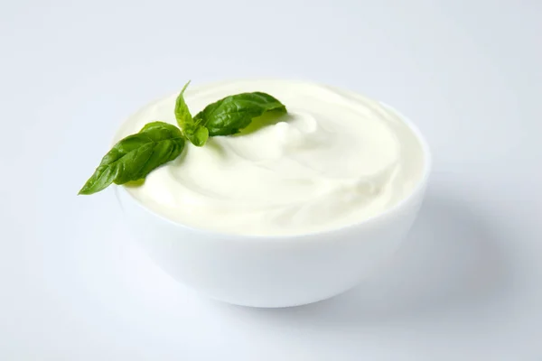 Bowl of fresh sour cream with basil on white background — Stock Photo, Image