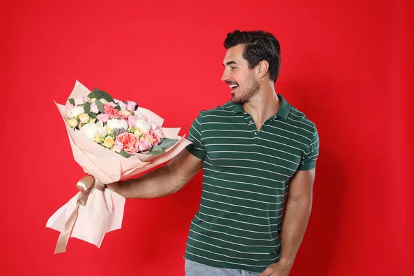 Joven hombre guapo con hermoso ramo de flores sobre fondo rojo —  Fotos de Stock