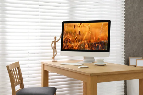 Modern PC on table near window with blinds in room — Stock Photo, Image