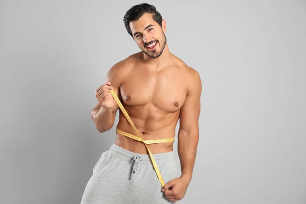 Joven con cuerpo delgado usando cinta métrica sobre fondo gris — Foto de Stock