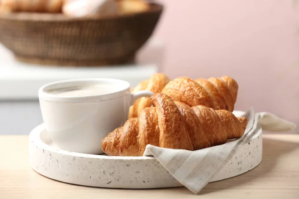 Teller mit frischen Croissants serviert mit Tasse Kaffee auf Holztisch drinnen, Nahaufnahme. französisches Gebäck — Stockfoto