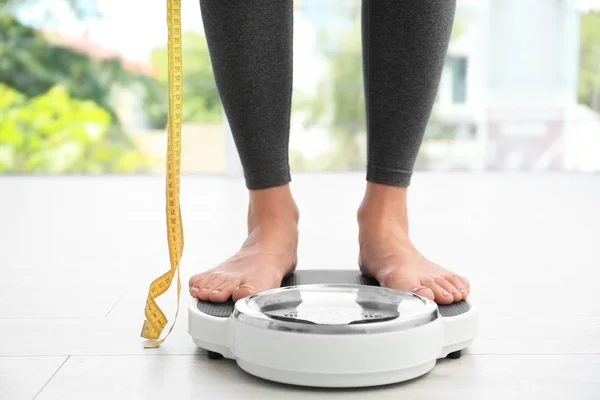 Vrouw met tape staande op schubben binnenshuis. Overgewicht probleem — Stockfoto