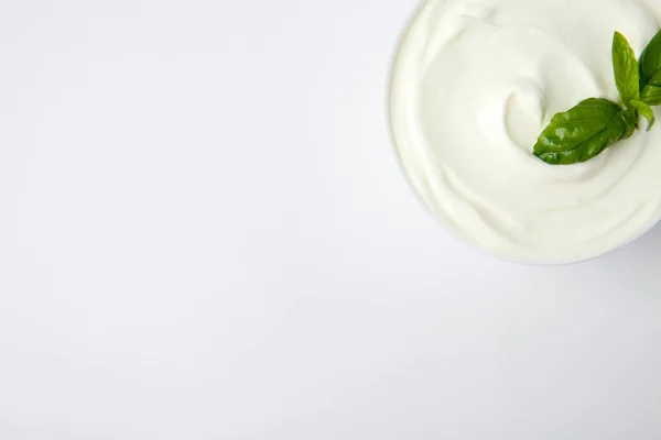 Bowl of fresh sour cream with basil on white background, top view — Stock Photo, Image