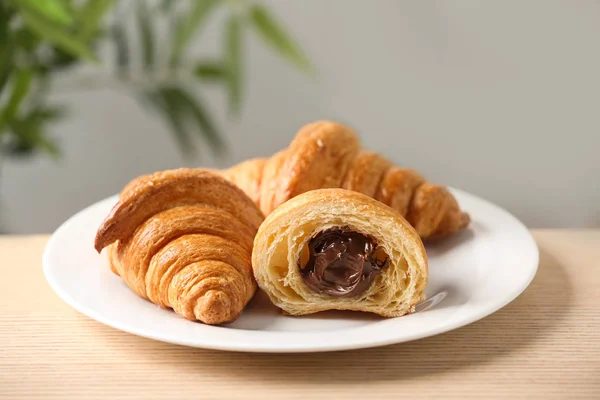 Plate of fresh croissants with chocolate stuffing on wooden table indoors, closeup. French pastry — Stock Photo, Image