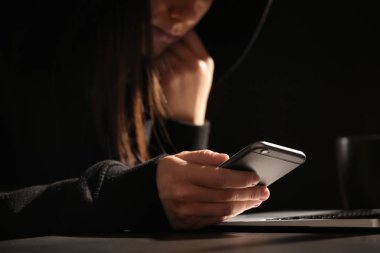 Karanlıkta dizüstü bilgisayar ile masada akıllı telefon kullanan kadın, yakın çekim. Yalnızlık kavramı