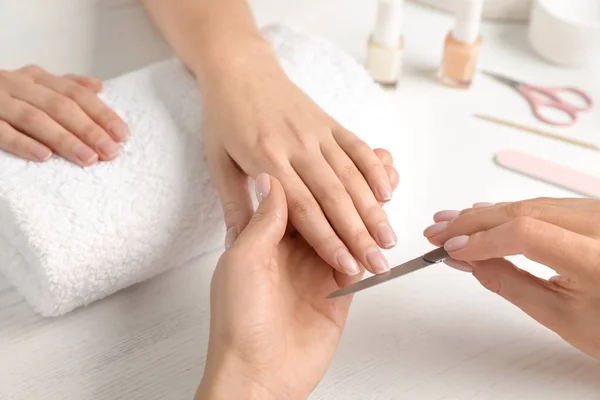 Manicurist filing client\'s nails at table, closeup. Spa treatment