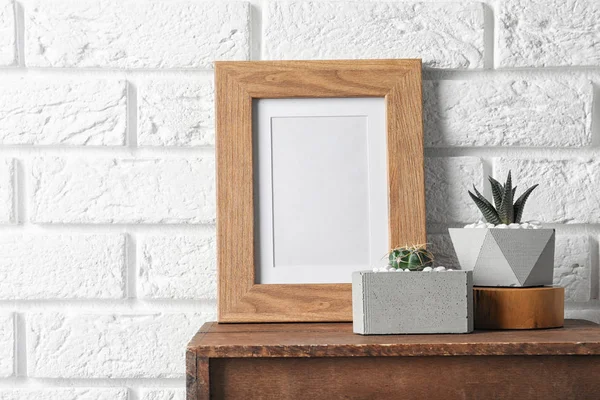 Marco en blanco y plantas suculentas en el gabinete de madera cerca de la pared de ladrillo blanco, espacio para el diseño. Decoración del hogar — Foto de Stock