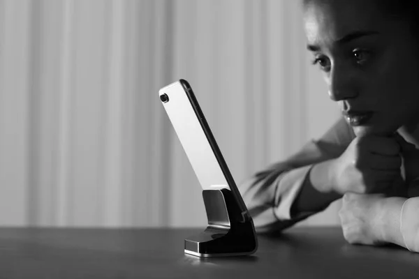 Mujer solitaria con teléfono móvil en la mesa en el interior, espacio para el texto. Efecto blanco y negro —  Fotos de Stock