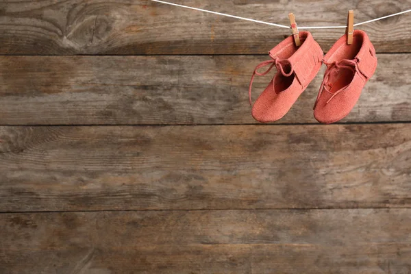 Pair of shoes on laundry line against wooden background, space for text. Baby accessories — Stock Photo, Image
