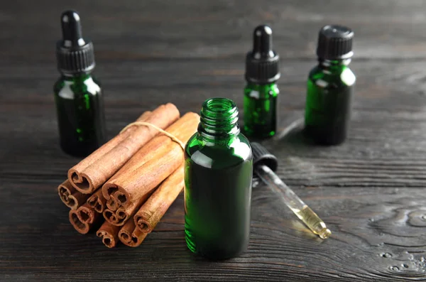 Bottles with essential oil and cinnamon sticks on black wooden table — Stock Photo, Image