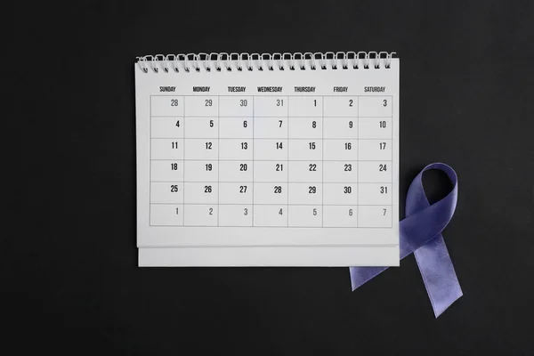 Purple awareness ribbon and calendar on black background, top view