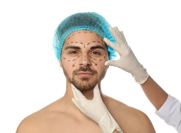 Doctor examining man's face with marker lines for plastic surgery operation on white background — Stock Photo, Image