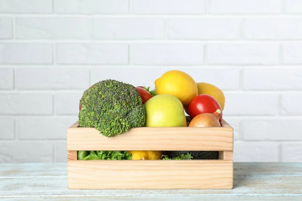 Wooden crate with fruits and vegetables on table near white brick wall, space for text