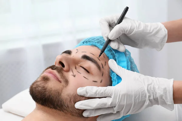 Dokter menggambar tanda di wajah manusia untuk operasi bedah kosmetik di klinik. — Stok Foto