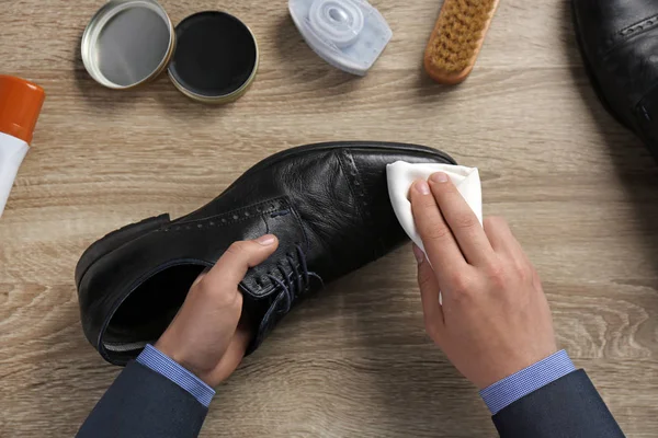 Man cleaning leather shoe at wooden table, top view