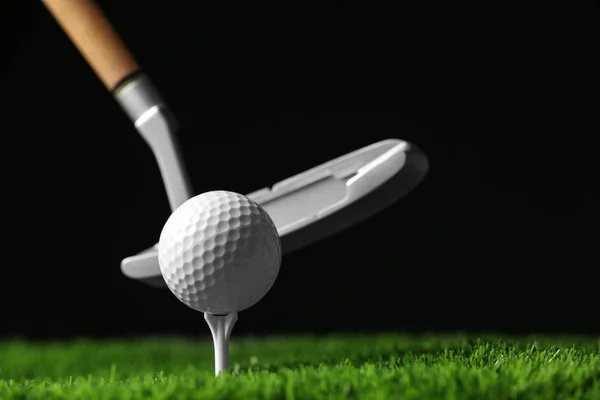 Bater bola de golfe com clube na grama artificial contra fundo preto, espaço para texto — Fotografia de Stock