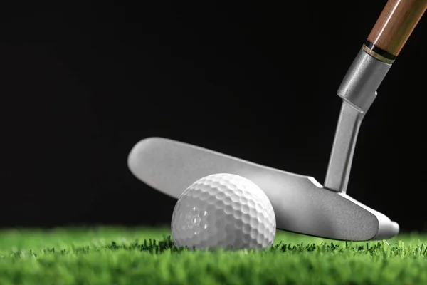 Bater bola de golfe com clube na grama artificial contra fundo preto, espaço para texto — Fotografia de Stock
