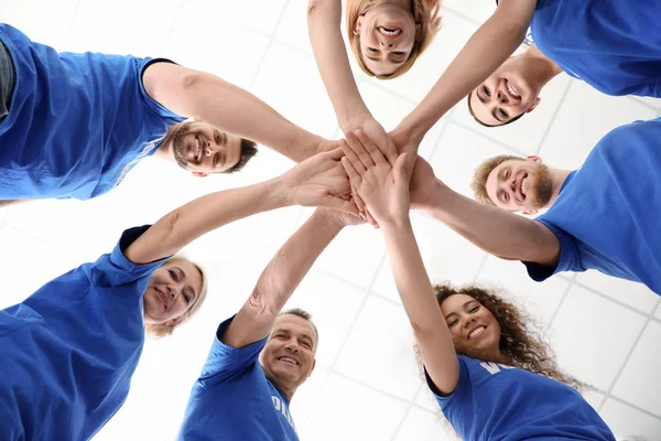 Team von Freiwilligen, die ihre Hände auf hellem Hintergrund zusammenlegen, Ansicht von unten — Stockfoto