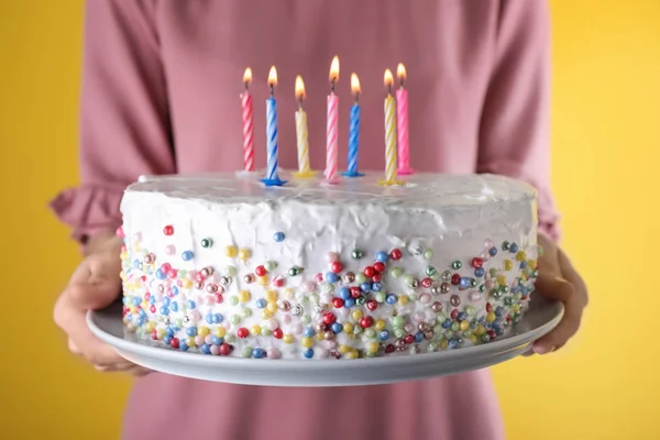 Жінка тримає торт на день народження з палаючими свічками на жовтому фоні, крупним планом — стокове фото