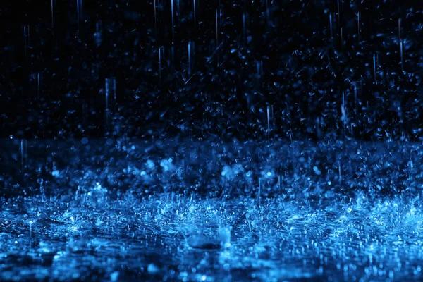 Lluvia fuerte cayendo sobre el suelo sobre fondo oscuro, tonificado en azul — Foto de Stock