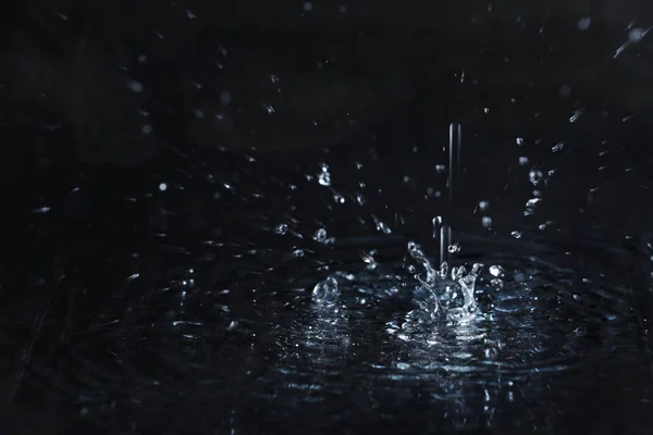 Rain drop falling down into puddle on dark background — Stock Photo, Image