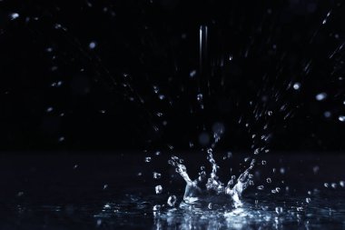 Karanlık arka planda su birikintisine düşen yağmur damlası