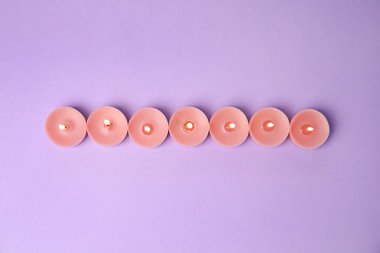 Mor arka plan üzerinde yanan balmumu dekoratif mumlar, düz yatıyordu