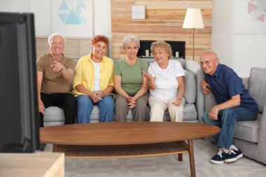 Mutlu yaşlı insanlar oturma odasında birlikte Tv izliyor