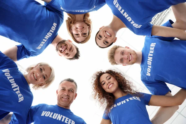 Team of volunteers joined in circle on light background, bottom view