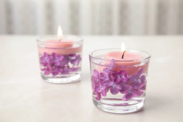 Glashållare med vatten, lila blommor och brinnande ljus på ljusbord, utrymme för text — Stockfoto