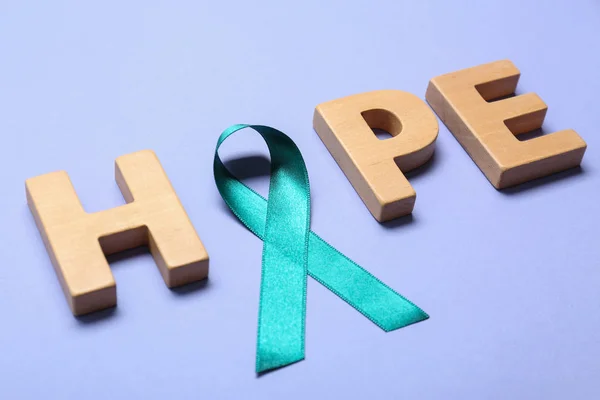 Palabra Esperanza hecha de letras de madera y cinta de conciencia verde azulado sobre fondo lila. Símbolo de cuestiones sociales y médicas — Foto de Stock