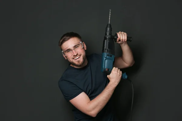 Jeune homme de travail avec marteau rotatif sur fond sombre — Photo