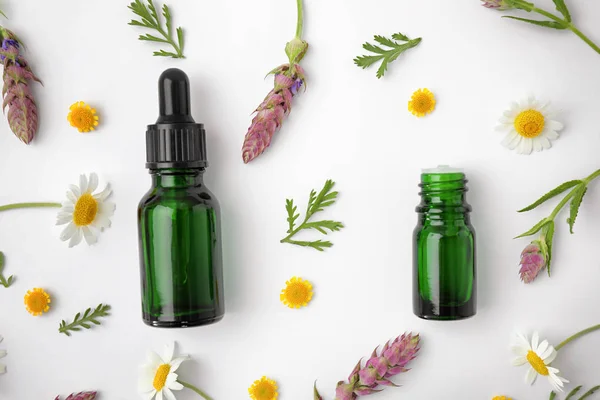 Bottles of different essential oils and wildflowers on white background, top view