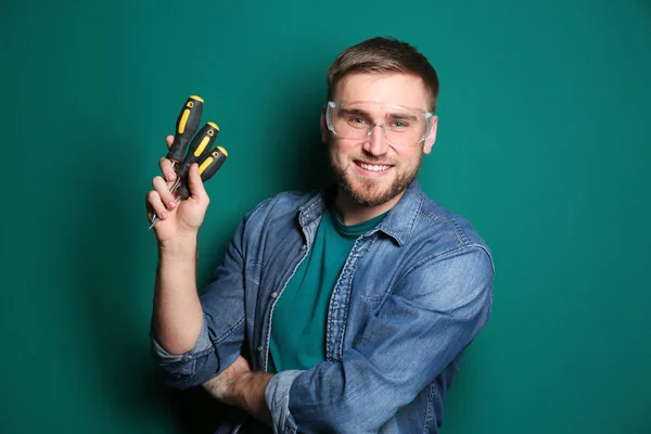 Young working man with screwdrivers on green background — Stock Photo, Image