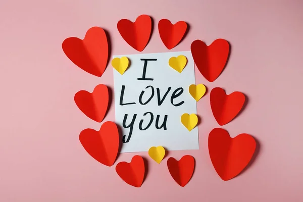 Rama wykonana z papierowych serc i kart z frazą I Love You na różowym tle, płaskie lay — Zdjęcie stockowe