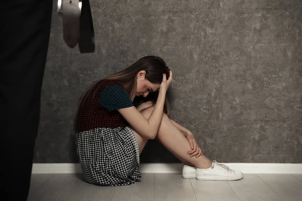 Man with belt standing in front of crying woman indoors, space for text. Stop sexual assault