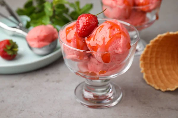 Delicioso helado rosa servido con jarabe y fresa en un tazón de postre sobre una mesa gris — Foto de Stock